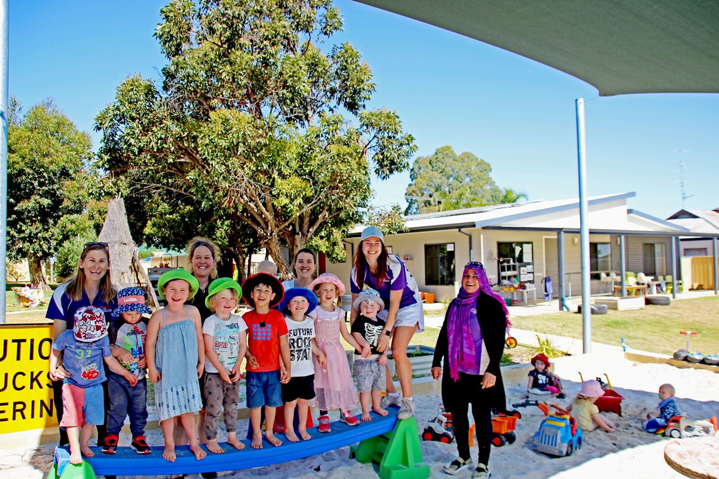 A group of toddlers and pre schoolers in bright clothing smile with their carers