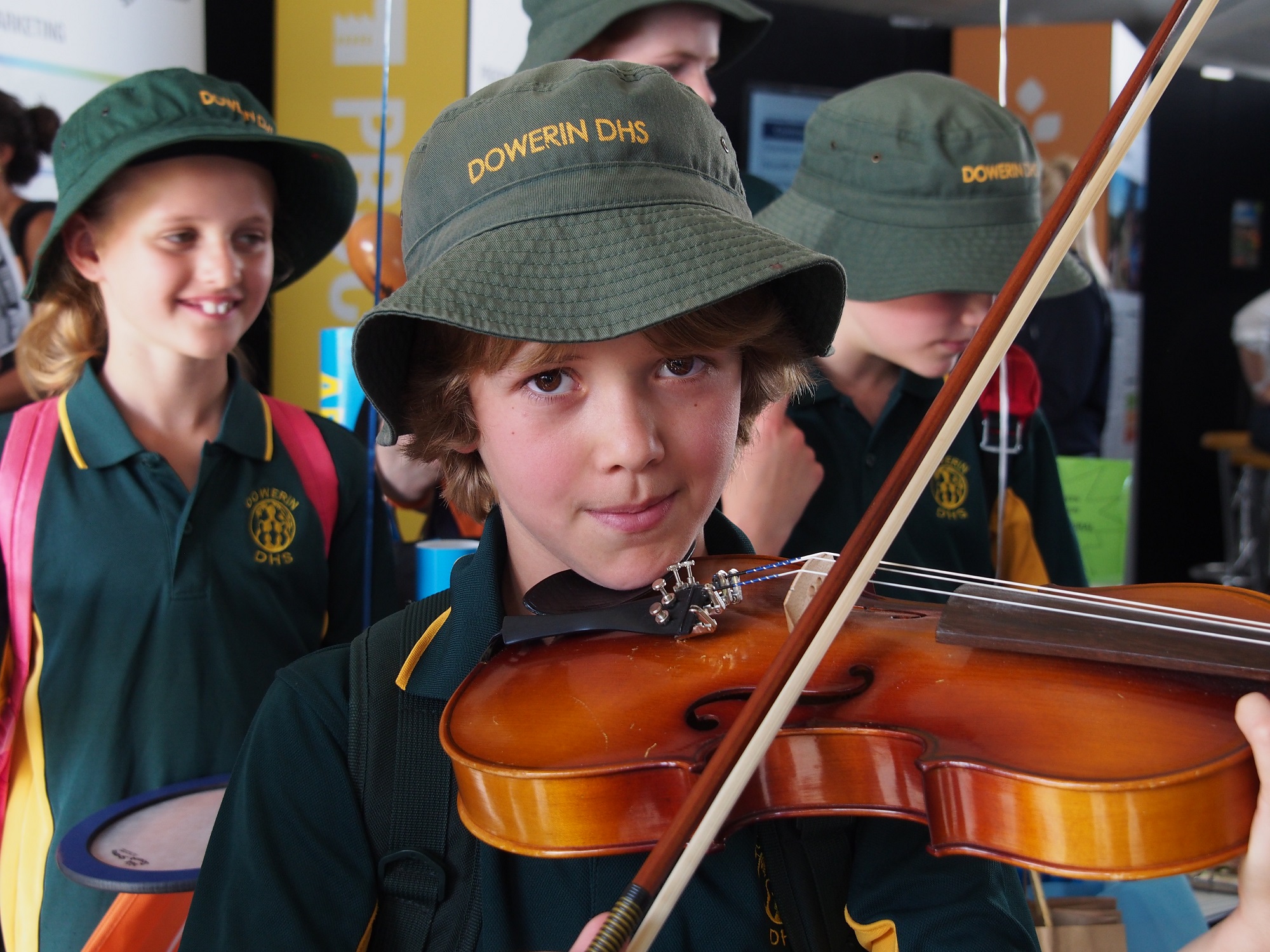 A young school boy wearing a green hat plays the violin