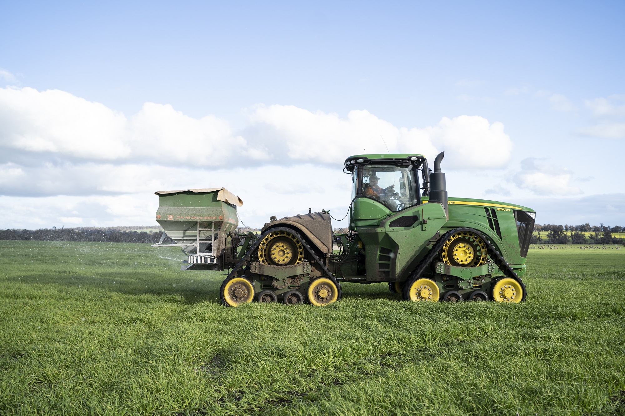A green tractor spreads urea fertiliser in a paddock