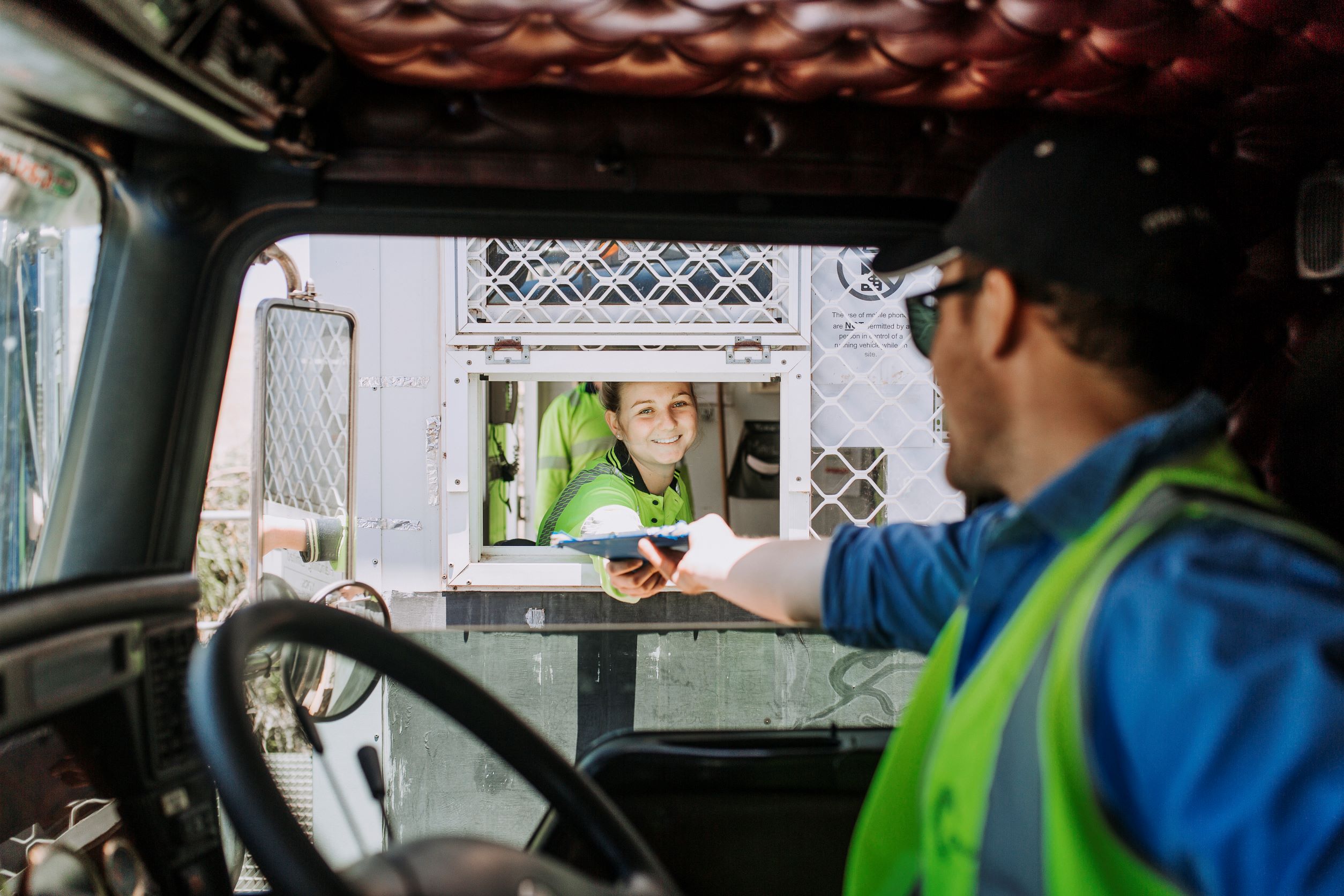 A truck driver handing a clipboard to a girl through the window of the sample hut