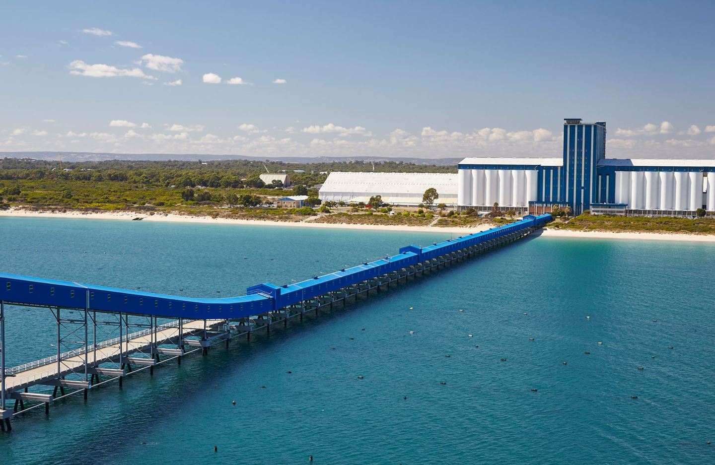 A large blue and white terminal has a long blue jetty stretching out to sea