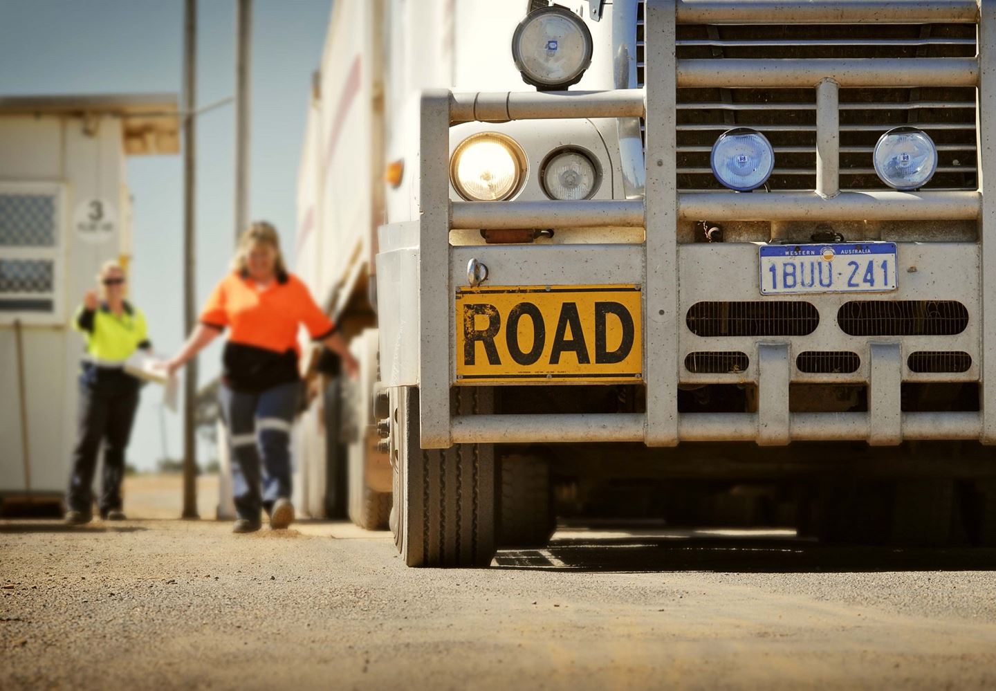 Two men wearing hi vis stand to the side of a large road train truck